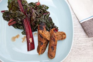 Two vegetarian sausages on a white plate with grilled chard.