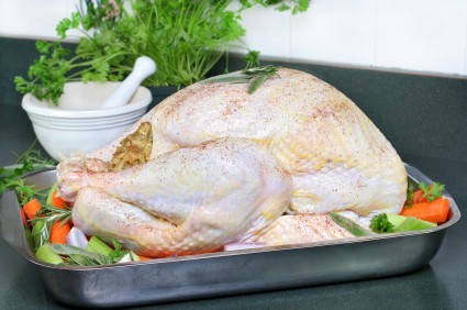 A raw turkey in a roasting tin with a selection of vegetables.