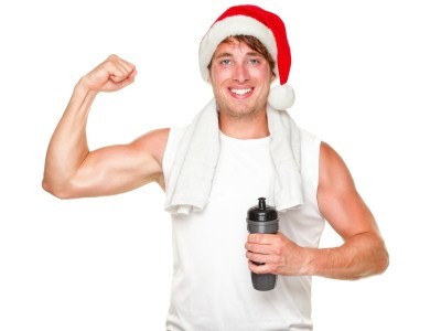 A man flexing his right bicep while holding a water bottle and wearing a Christmas hat.