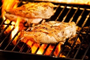 Two grilled chicken breasts on a barbecue.