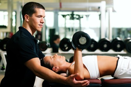 A male personal trainer spotting a female whilst performing dumbbell chest presses.