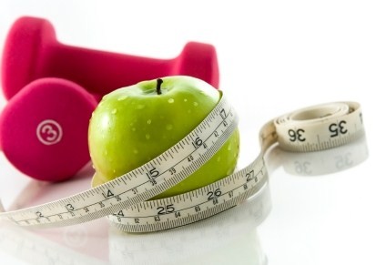 A green apple wrapped in a tape measure next to a pair of pink dumbbells.