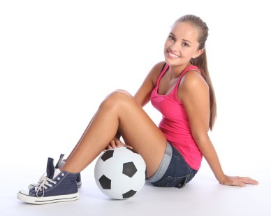 A teenage girl sitting next to a soccer ball on a white background.