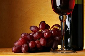 A bunch of red grapes next to a glass and bottle of red wine.