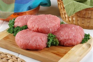 A selection of raw chicken burgers on a chopping board.