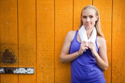 A woman relaxing against a wooden with a towel after exercise.