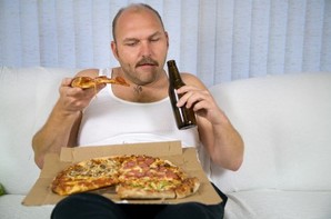 An overweight man drinking beer and eating pizza.