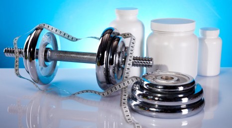 A set of dumbbells and weight plates next to some white bottles of fat burners.