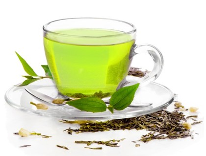 A g;ass cup of green tea surrounded by green tea leaves.