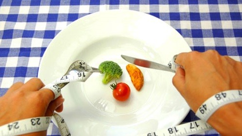 A person eating vegetables with a tape measure wrapped around their hands.