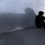 A man with his hood up, sitting against a wall.