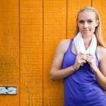 A woman relaxing against a wooden with a towel after exercise.
